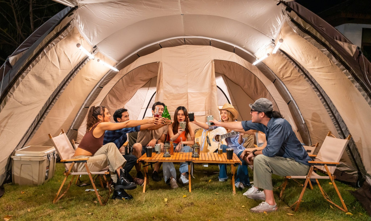 A man and a woman are sitting outdoors by a ten with a solar panel, a portable solar power station and a few camping devices.