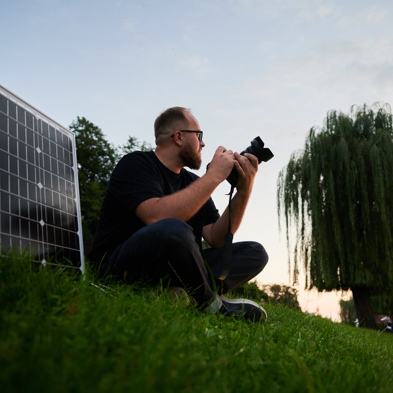 Filmmaker sitting at a picnic table outdoors with a camera, light, laptop and portable solar power station.