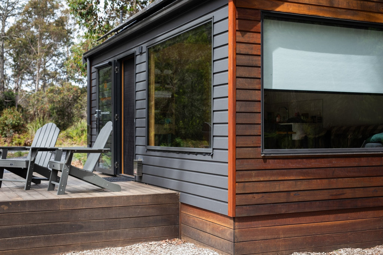 A woman seated at a small table inside a tiny house or small ADU, using a portable solar power station to power with a heater, a split mini A/C, and a computer..
