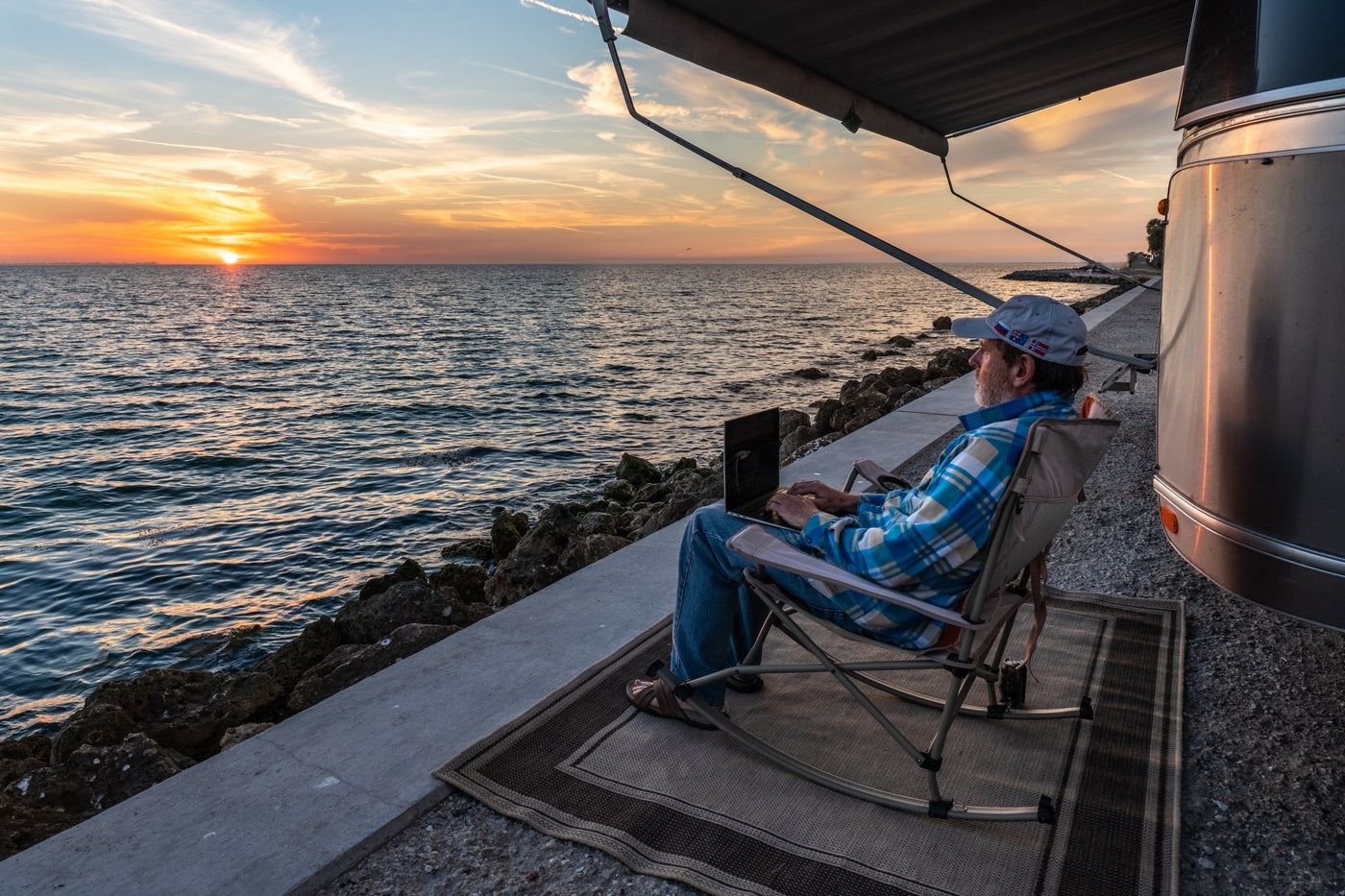 Person using a laptop by an RV by the ocean at sunset